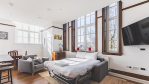 A bedroom with a bed, a desk, a chair, and large windows. - Stylish Historic Acton Apartment (London)