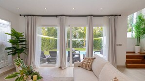 Un salon moderne doté d’un grand canapé, d’une table basse et offrant une vue sur une piscine et un jardin grâce à de grandes fenêtres du sol au plafond.