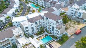 A residential complex with multiple apartment buildings, a swimming pool, and a road with parked vehicles.