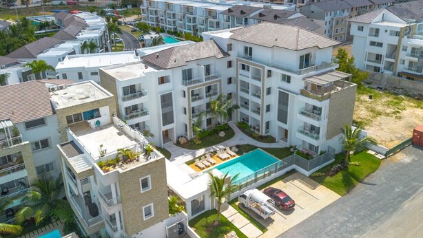 A modern apartment complex with multiple buildings, a swimming pool, and a parking area.