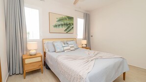 A bedroom with a bed, two bedside tables, a nightstand, a ceiling fan, and a window with curtains.