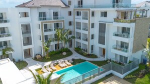 A multi-story residential building with balconies, a swimming pool, and landscaped gardens.