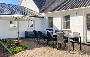 Une terrasse avec une table et des chaises, un parasol et un pot de fleurs.