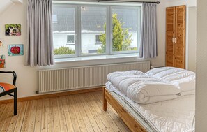Une chambre à coucher avec un lit, un plancher en bois, une fenêtre avec des rideaux, un radiateur et une armoire.