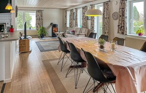 Cozinha moderna com fogão embutido, área de refeições com mesa comprida e cadeiras, e um espaço de estar aconchegante com sofá.