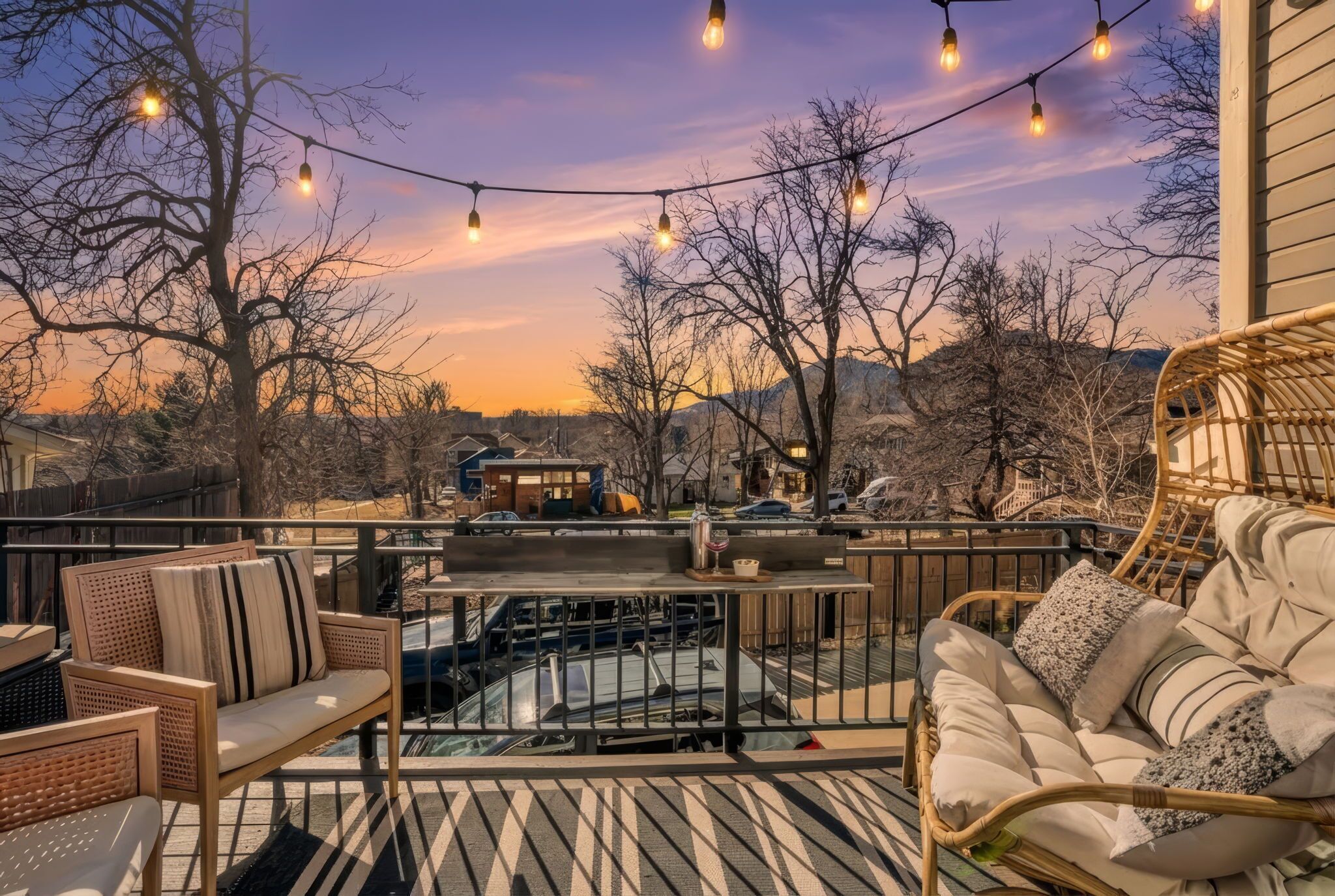 A deck with wicker furniture, string lights, and a view of a residential area.