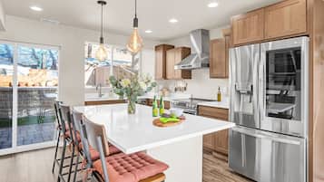 A modern kitchen with a large island, stainless steel appliances, wooden cabinets, and a seating area with cushioned chairs.