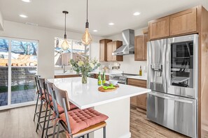 Cocina moderna con una isla grande, electrodomésticos de acero inoxidable, armarios de madera y un rincón de estar con sillas acolchadas.