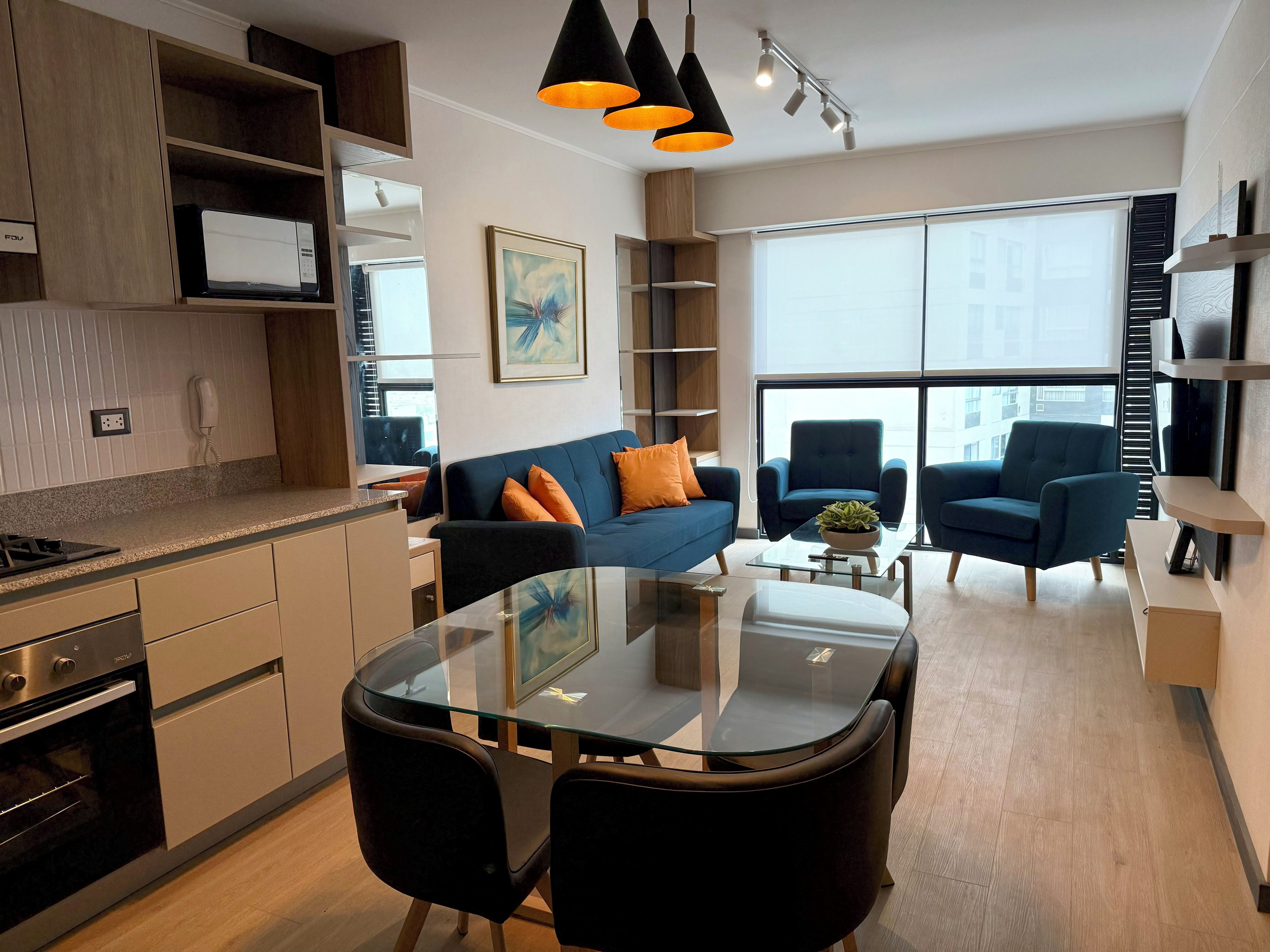 A modern kitchen with built-in appliances, a dining area with a glass table, and a living space with a sofa and armchairs.