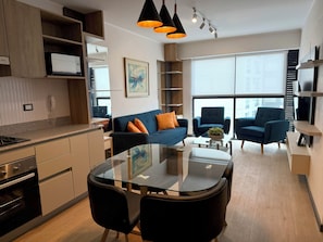 A modern kitchen with built-in appliances, a dining area with a glass table, and a living space with a sofa and armchairs. - APT STYLE - MAGDALENA (Lima)