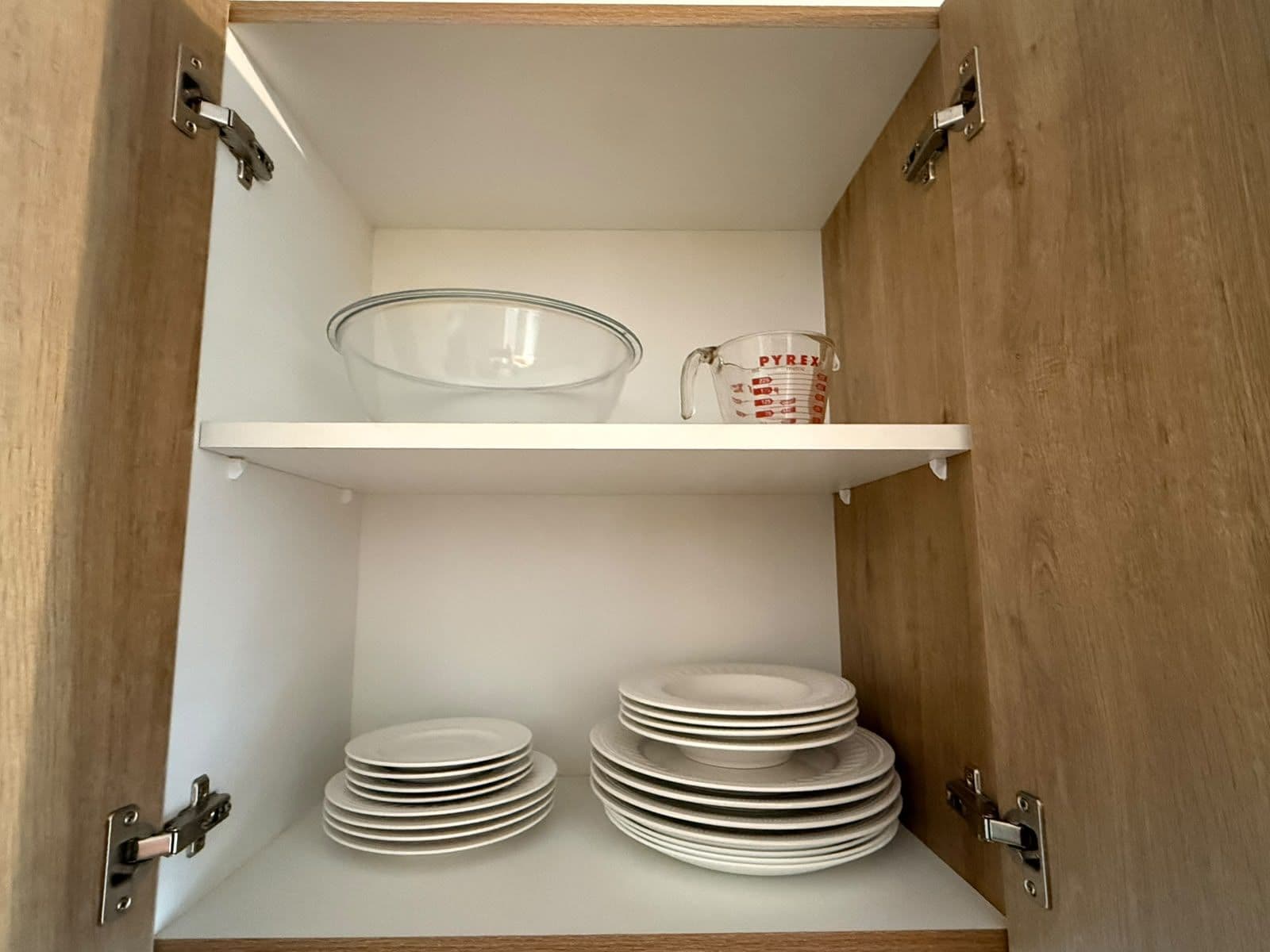 A kitchen cabinet with white shelves, a Pyrex measuring cup, and stacked plates.