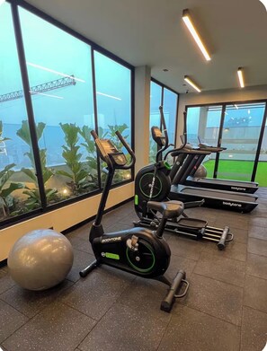 Ein Fitnessstudio mit Laufbändern, einem Übungsball und großen Fenstern mit Blick auf eine Grünfläche.