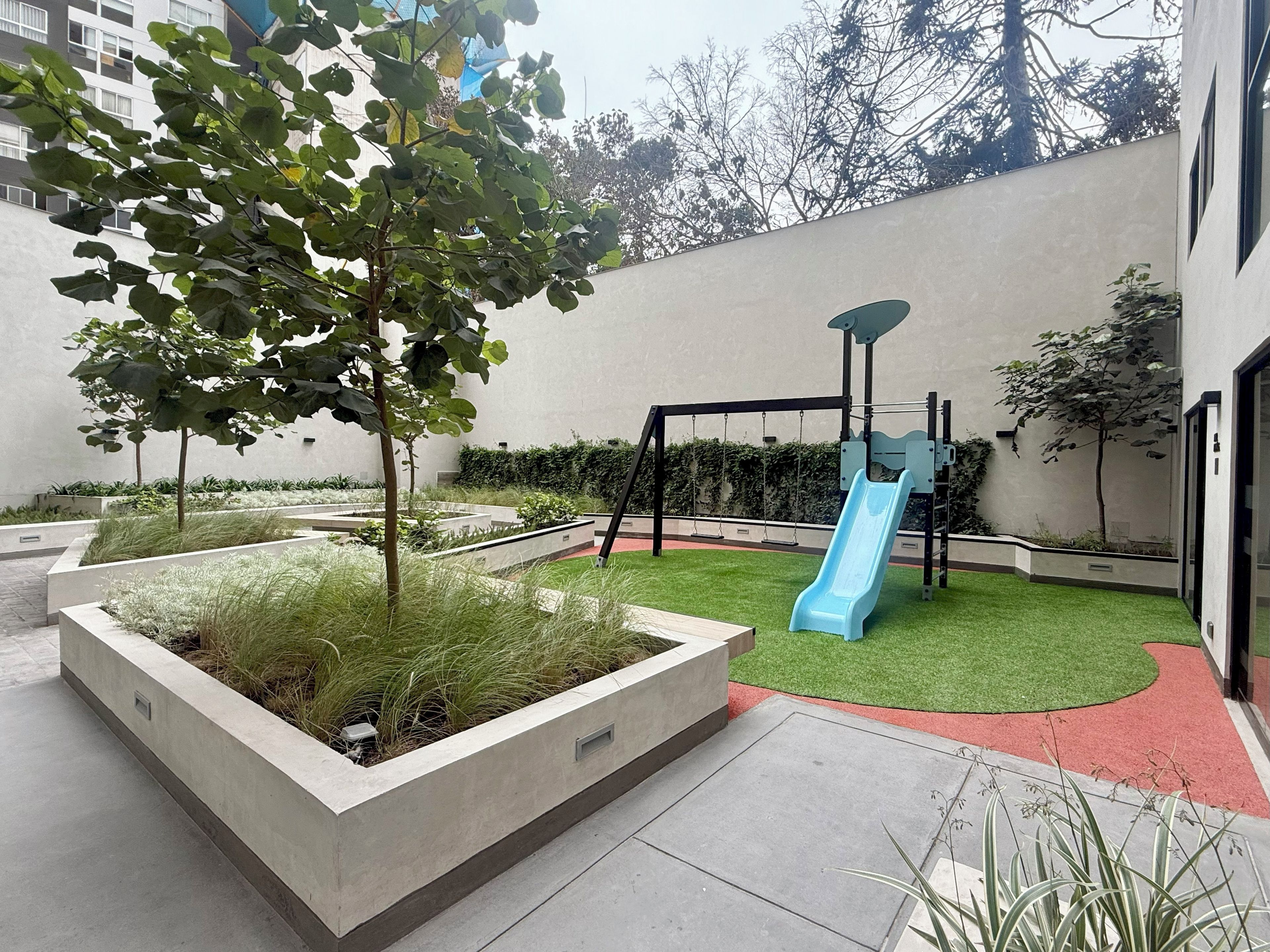A playground with a blue slide and swings, surrounded by landscaped areas with grass and plants.