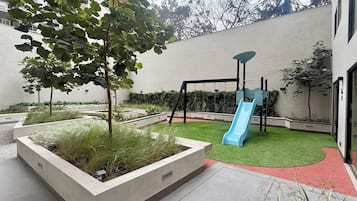 A playground with a blue slide and swings, surrounded by landscaped areas with grass and plants.