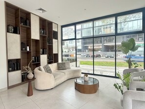 Una sala moderna con un ventanal grande, un sofá, una mesa de centro y estanterías empotradas con varios objetos decorativos.