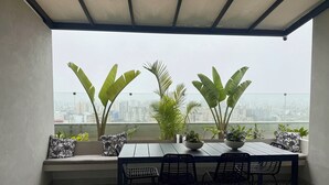 Un balcó amb taula i cadires, plantes en testos i vista a la ciutat.