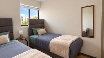 Habitación de hotel con dos camas, una mesita de noche, una lámpara, una ventana con persianas y un espejo en la pared.
