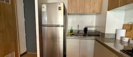 A compact kitchen with a stainless steel refrigerator, wooden cabinets, a granite countertop, and a built-in sink.