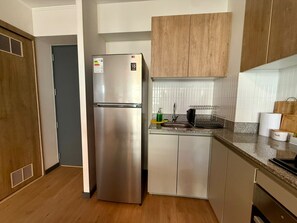 A compact kitchen with a stainless steel refrigerator, wooden cabinets, a granite countertop, and a built-in sink. - APT STYLE - MAGDALENA (Lima)