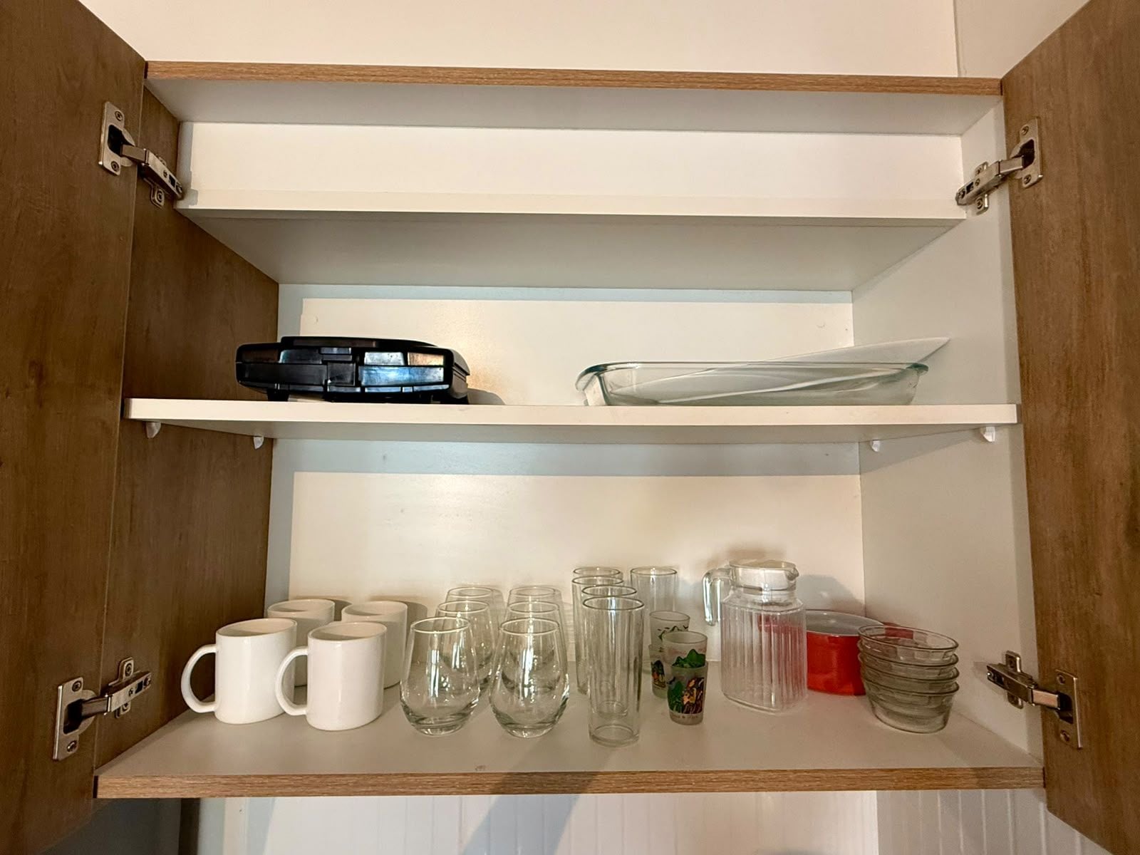 Un mueble con dos estantes, uno con un objeto negro y el otro con cristalería transparente y una taza blanca.
