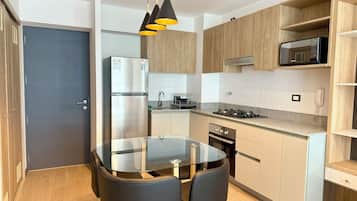 A modern kitchen with a glass dining table, black chairs, wooden cabinets, a stainless steel refrigerator, and a microwave on the countertop.