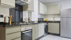Een moderne keuken met lichte kastjes, een inbouwoven, een magnetron en een wasmachine.