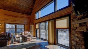 A spacious living room with leather sofas, a coffee table, and large windows offering a view of the outdoors.