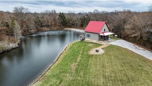 A house with a red roof, a covered porch, and a small pond in the foreground.