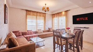 Una sala de estar con sofá, mesa de centro, mesa de comedor, sillas y televisor montado en la pared.