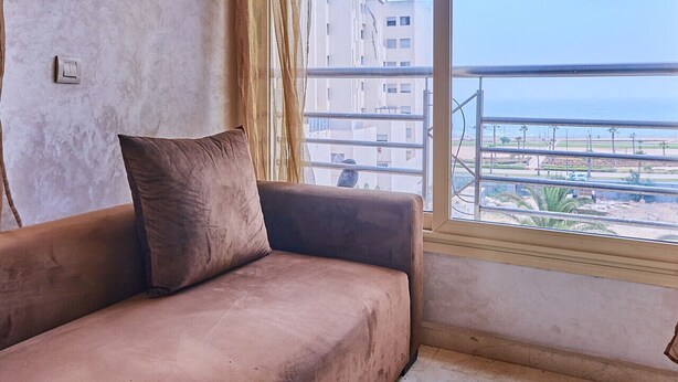 Una habitación con un sofá marrón, un ventanal con vistas a edificios y una masa de agua.