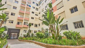 Un edificio residencial de varios pisos con balcones, entrada protegida por un portón y un jardín ajardinado.