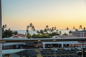 A hotel parking lot with multiple cars, palm trees, and a view of the ocean at sunset. - Sun Style & Location Viva Jaco Condo (Jacó)