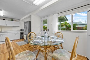 Una cocina moderna con armarios blancos, un refrigerador de acero inoxidable y una zona de comedor con una mesa de vidrio y sillas de madera.