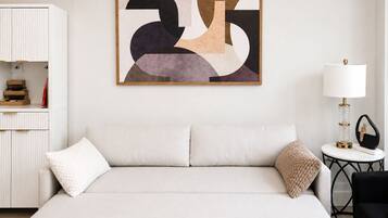 Une chambre d’hôtel avec un grand lit, une armoire blanche, une petite table ronde avec une lampe et un tableau abstrait accroché au mur.