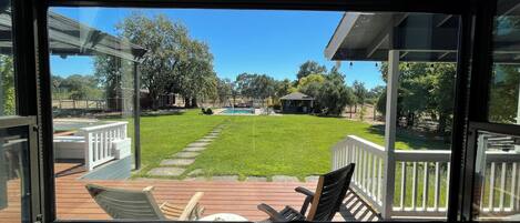 A view from inside a room with a large window overlooking a backyard with a pool, deck, and outdoor furniture.