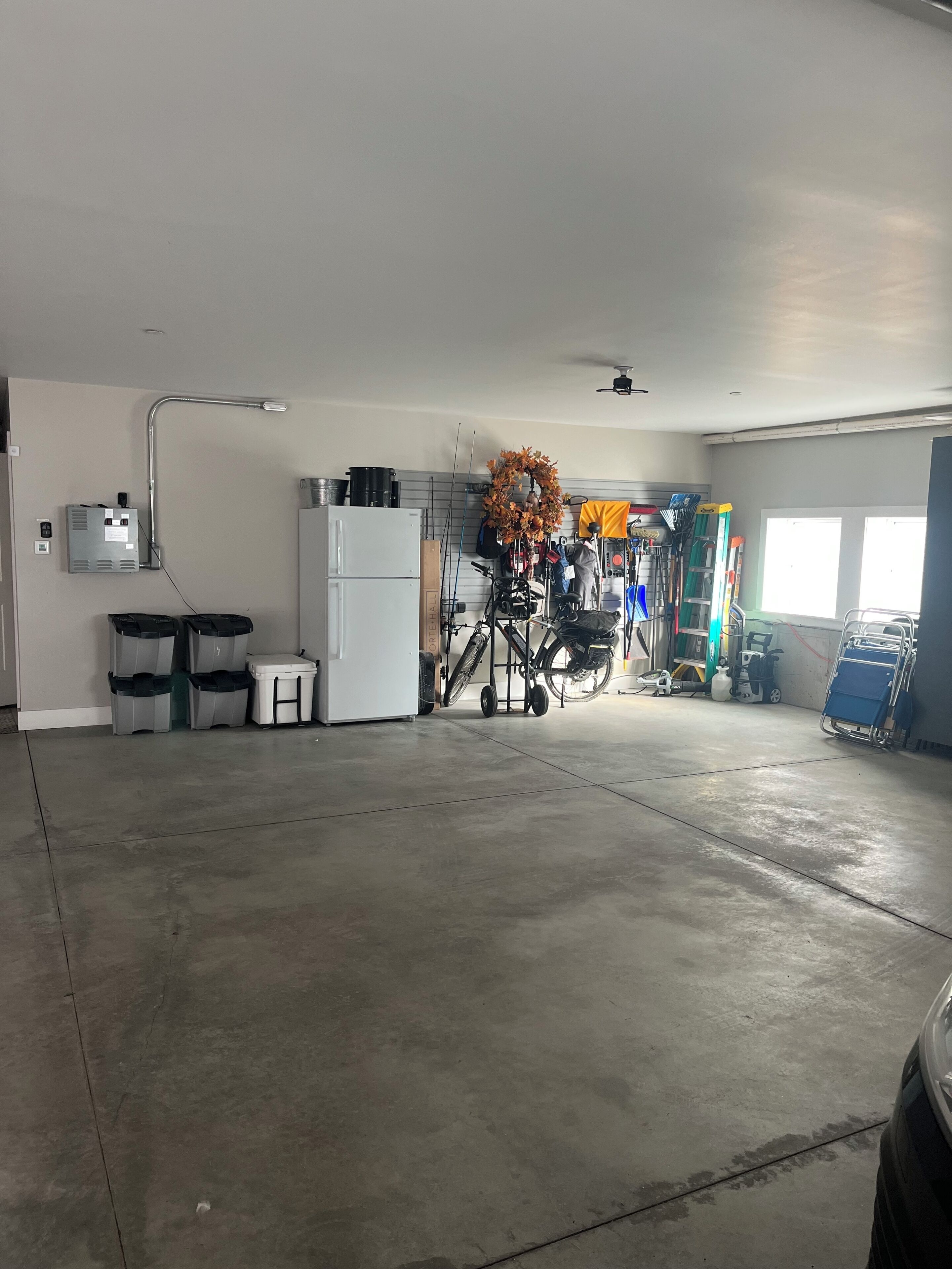 A spacious garage with a concrete floor, a white refrigerator, a workbench, and various tools and equipment.