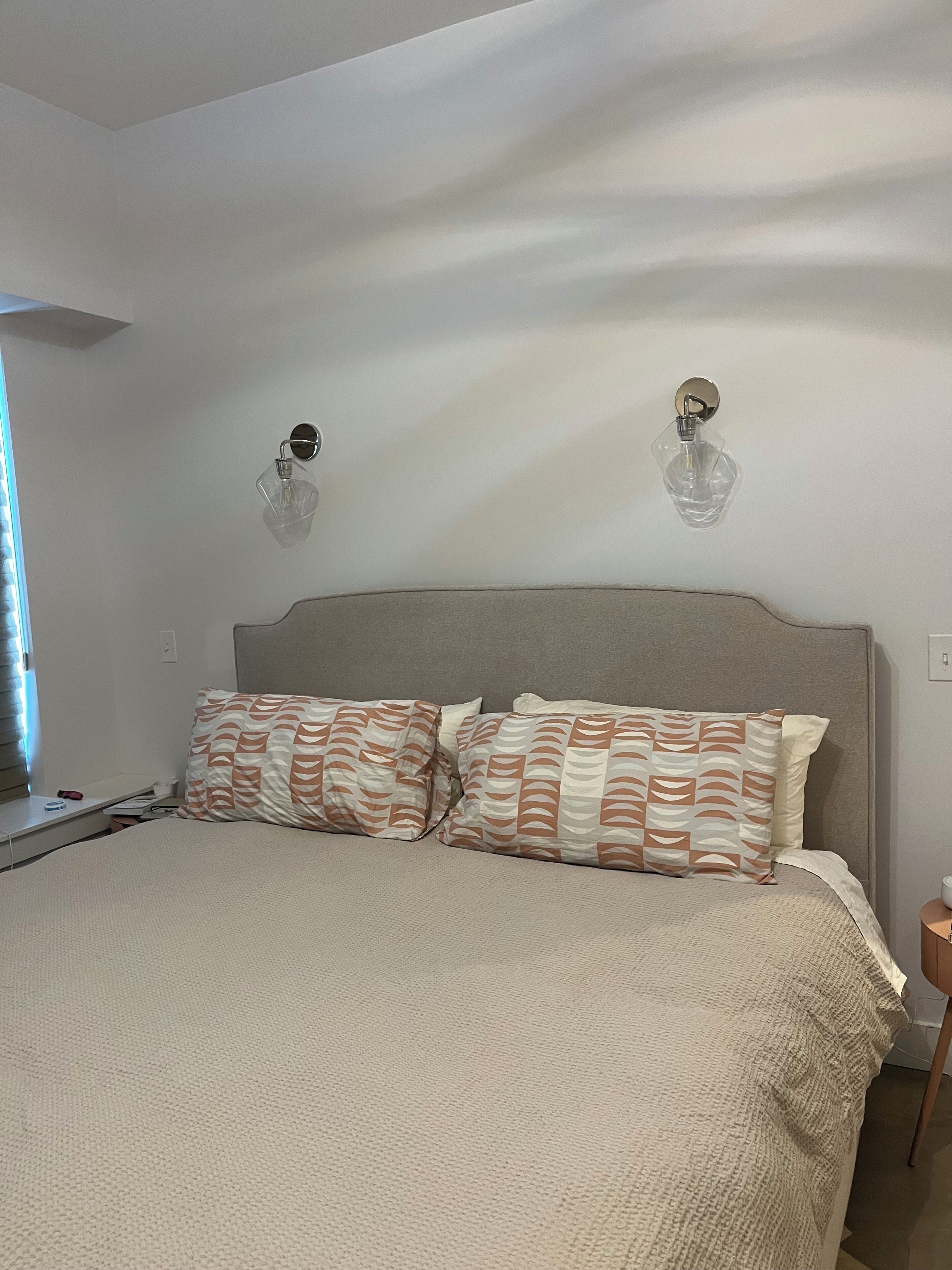 Een slaapkamer met een bed, twee wandlampen en een nachtkastje.