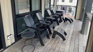 A covered outdoor seating area with modern chairs and tables, large windows, and a view of the street. - Steps from Old Port. New, Beautifully Appointed Home. Sleeps up to 11. (Portland)