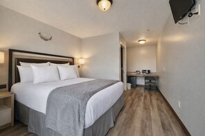 A hotel room with a bed, bedside table, desk, and a television. - Siesta Inn (Salt Lake City)