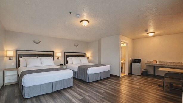 A hotel room with two beds, a desk, a chair, a microwave, and a sink. - Siesta Inn (Salt Lake City)