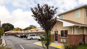 A motel with a parking lot, a single-story building, and a tree in front. - Siesta Inn (Salt Lake City)