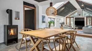 A modern living room with a large wooden dining table, a built-in wood stove, and a large window providing natural light. - Gorgeous home in Vestervig with WiFi (Vestervig)