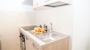 Une cuisine compacte dotée d’un four encastré, d’un évier en acier inoxydable et d’un petit plan de travail.