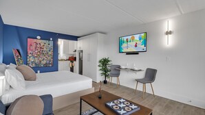 Una habitación de hotel moderna con una cama, una zona de estar con una mesa de centro, un televisor y obras de arte en las paredes.