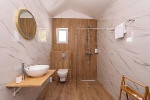 Ein modernes Badezimmer mit einem großem, ovalen Waschbecken, einer Toilette, einer Duschkabine aus Glas und einem Holzkosmetikschrank.