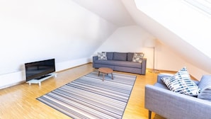 A modern loft apartment with a high ceiling, a grey sofa, a flat-screen TV, and a striped rug. - Ferienresidenz Hinterzarten FEWO 11 (Hinterzarten)