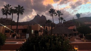 A resort with palm trees, a mountain, and buildings with red-tiled roofs.