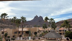 A pool area with a mountain in the background, palm trees, and a thatched-roof structure.