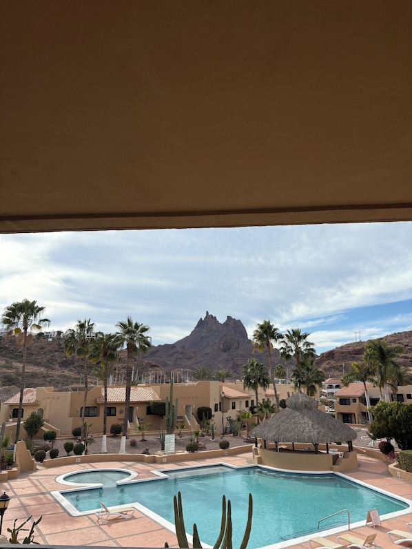 A pool area with a mountain in the background, palm trees, and a thatched-roof structure.