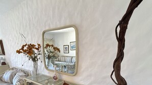 A room with a white textured wall, a glass-top console table with a vase of flowers, a mirror, a wicker sofa, and a potted plant.